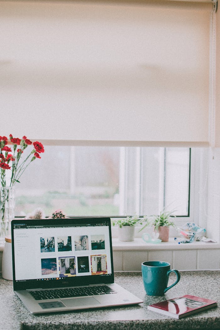 services-04 A cozy home office setup with a laptop, coffee mug, and flowers by a sunlit window, ideal for remote work.