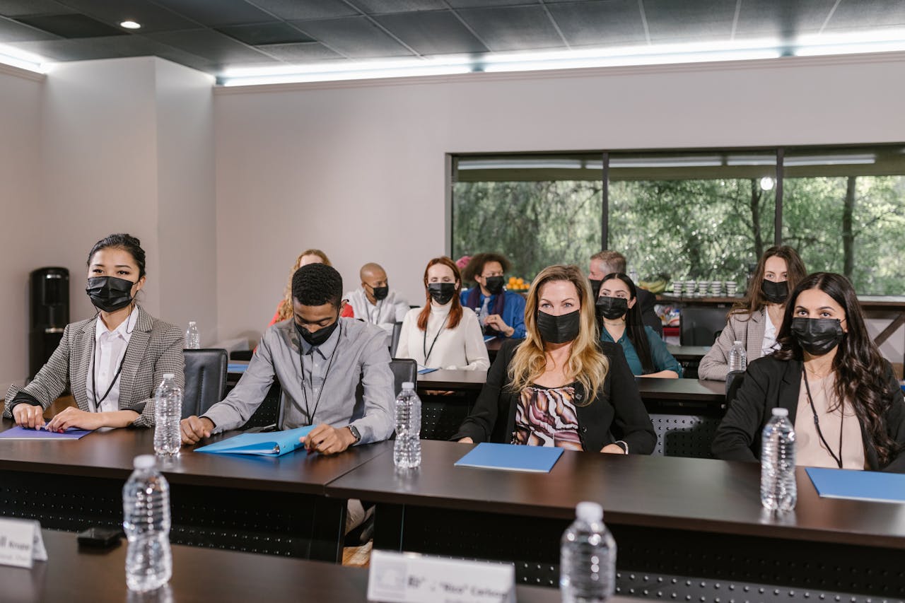 A group of masked professionals in a business meeting setting, maintaining social distance.
