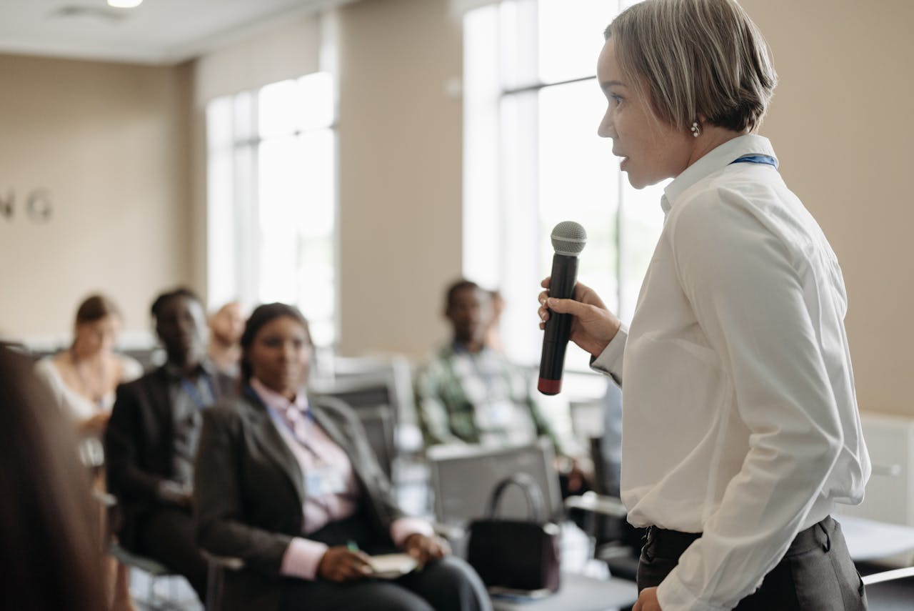 services-02 Side view of a businesswoman holding a microphone while addressing an audience at a conference.